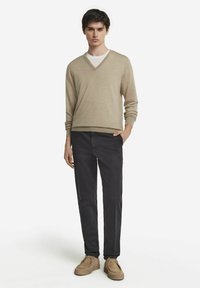 Beige V-hals tröja, svarta byxor och beige skor. Tröjan har en mjuk textur; byxorna är åtsittande; skorna har en enkel design.