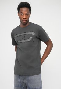 T-shirt di cotone grigio scuro con stampa grafica con le parole "PROPERTY OF" in nero, maniche corte e scollo rotondo.