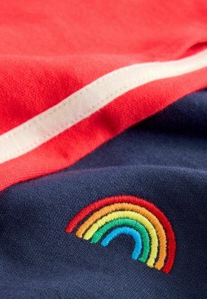 Tessuto rosso con una striscia bianca sovrapposta a un tessuto blu navy, caratterizzato da un colorato design ricamato a forma di arcobaleno. Texture morbida, tessuto stratificato.