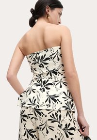 Mouwloze peplumtop in crèmekleurige stof met een zwart bloemenpatroon, met een aansluitend lijfje en een zachte, gestructureerde afwerking.