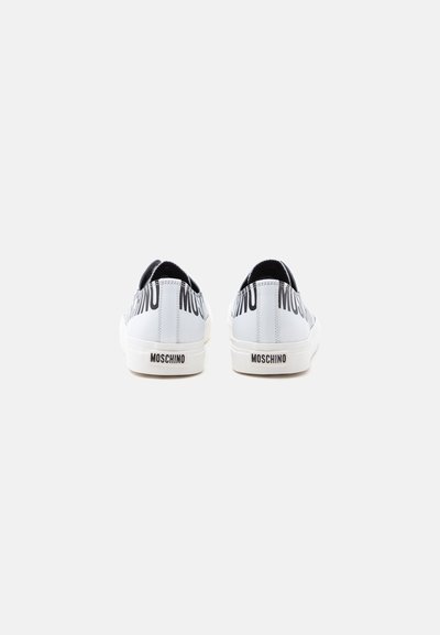 Ζευγάρι λευκά sneakers Moschino που φαίνονται από πίσω, με μαύρα λογότυπα στη φτέρνα και στο επάνω μέρος των παπουτσιών.