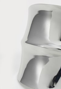 Metallisch zilveren decoratief object met een golvende, bolvormige vorm en een gladde, reflecterende oppervlakte. Geen zichtbare patronen of accenten.