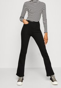 Mustat leveälahkeiset farkut korkealla vyötär�öllä ja etutaskuilla, yhdistettynä mustavalkoraidalliseen pitkähihaiseen ribbipaitaan. Rennot tennarit.