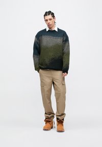 Πλεκτό πουλόβερ με διαβάθμιση σε πράσινο και γκρι, στρογγυλή λαιμόκοψη· συνδυασμένο με μπεζ παντελόνι cargo και καφέ δερμάτινα μποτάκια με κορδόνια. Απλή, άνετη εφαρμογή.