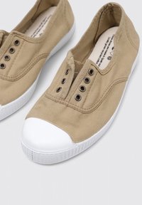 Bottines en toile beige à enfiler avec embout et semelle en caoutchouc blanc. Possède cinq œillets en métal le long du dessus du pied sans lacets. Texture lisse.