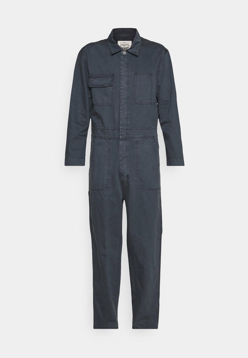 Combinaison bleu foncé à manches longues avec col, fermeture avant par boutons et zip, poches poitrine et poches latérales, présentée sur fond blanc.