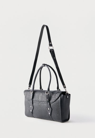 Μαύρη δερμάτινη τσάντα με υφή, με λαβές στην κορυφή και ρυθμιζόμενο μακρύ λουρί ώμου, αντίθετα σε απλό ανοιχτό φόντο.