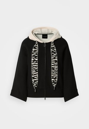 Svart huvtröja med kontrasterande beige insida, med snören i zebramönster och blixtlåsförslutning framtill.