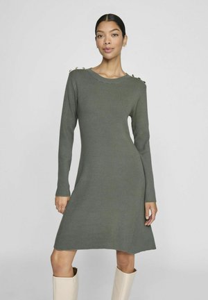 Robe en tricot à manches longues couleur vert olive avec texture côtelée, décolleté bateau et boutons dorés en accent sur l'épaule ; silhouette évasée.