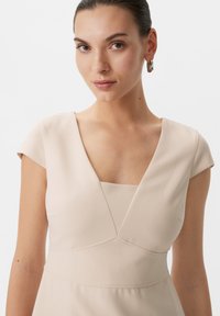 Hellbeiges Kleid mit tiefem V-Ausschnitt, Kurzärmeln und tailliertem Oberteil. Verfügt über ein nahtloses Design mit subtilen Nähten.