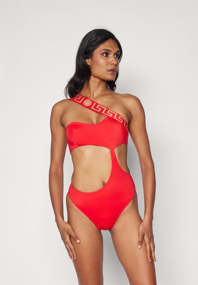 Maillot de bain une pièce rouge avec un design découpé, encolure asymétrique et motif clé grec doré sur la bretelle. Tissu lisse et extensible.