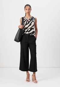 Sorte vide bukser i vid stil kombinert med en ermeløs topp med zebra-mønster i beige og svart. Modellen holder en svart skulderveske.