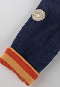 Manica in pile blu navy con polsini a costine a righe arancioni e gialle. Presenta una toppa rotonda con logo contenente testo e un'icona centrale.