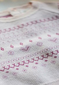 Pull en maille de couleur gris clair avec des motifs géométriques roses, doté d'un col rond et de détails en relief.