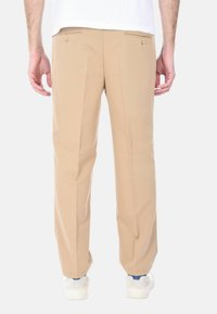 Pantaloni beige con design dritto, dotati di due tasche posteriori e tasche frontali in vita, realizzati in tessuto liscio. Indossati con sneakers bianche.