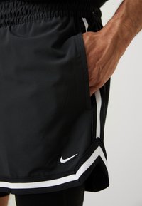 Black athletic shorts with elastic waistband, side pocket, white stripe accents, and Nike logo at the hem. Smooth fabric, loose fit.