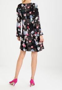 Mustakukkainen mekko pitkilla hihoilla, jossa on värikkäitä kukkakuoseja. levenevä helma ja yhdistetty kirkkaan vaaleanpunaisiin korkokenkiin.