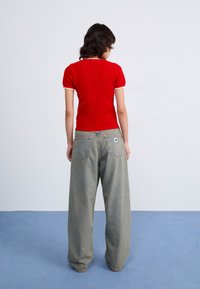 Red ribbed knit top with short sleeves, paired with light gray wide-leg jeans featuring back pockets and a brand logo patch.