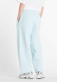 Pantalons de survêtement bleu clair avec une coupe décontractée, poches latérales et taille élastique. Associés à des chaussures de sport blanches et argentées.
