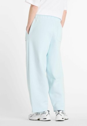 Pantalons de survêtement bleu clair avec une coupe décontractée, poches latérales et taille élastique. Associés à des chaussures de sport blanches et argentées.
