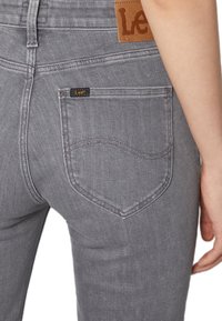 Grijze denim jeans met een slim fit, met achterzakken, een leren label met "Lee" branding, en subtiele stikseldetails.