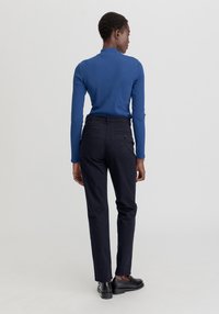 Niebieska bluzka z długim rękawem i wysokim kołnierzem, dopasowana, w zestawieniu z czarnymi spodniami slim-fit z tylnymi kieszeniami i gładką fakturą.