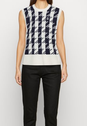 Haut sans manches en maille avec un motif géométrique noir et blanc, associé à un pantalon noir, montré sur une personne de la nuque aux hanches.