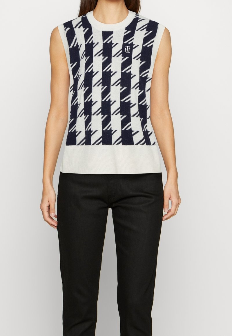Haut sans manches en maille avec un motif géométrique noir et blanc, associé à un pantalon noir, montré sur une personne de la nuque aux hanches.