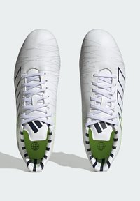 Zapatillas deportivas blancas con costuras en zigzag, detalles en negro y plantillas verdes. Presentan un diseño con cordones y un forro interior a rayas.