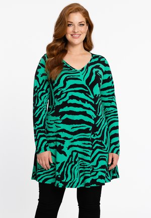 Langermige tuniek met een zwart en groen zebrapatroon, V-hals ontwerp, vloeiende stof en een relaxte pasvorm. Draagt met zwarte leggings.