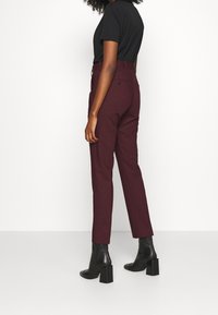 Burgundowe spodnie dopasowane ze smukłym krojem i detalami w formie zagniecenia, w parze z czarnymi botkami za kostkę. Gładki materiał o minimalistycznym designie.
