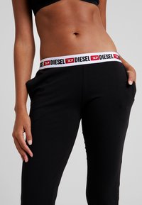 Schwarze Jogginghosen mit einem elastischen Bund in Weiß und Rot mit 'DIESEL'-Markenlogo, ausgestattet mit seitlichen Taschen und einem glatten, elastischen Stoff.
