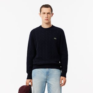 Navy cable-knit sweater with a round neckline, ribbed cuffs, and hem. Features a small green logo on the chest. Worn with light blue jeans.