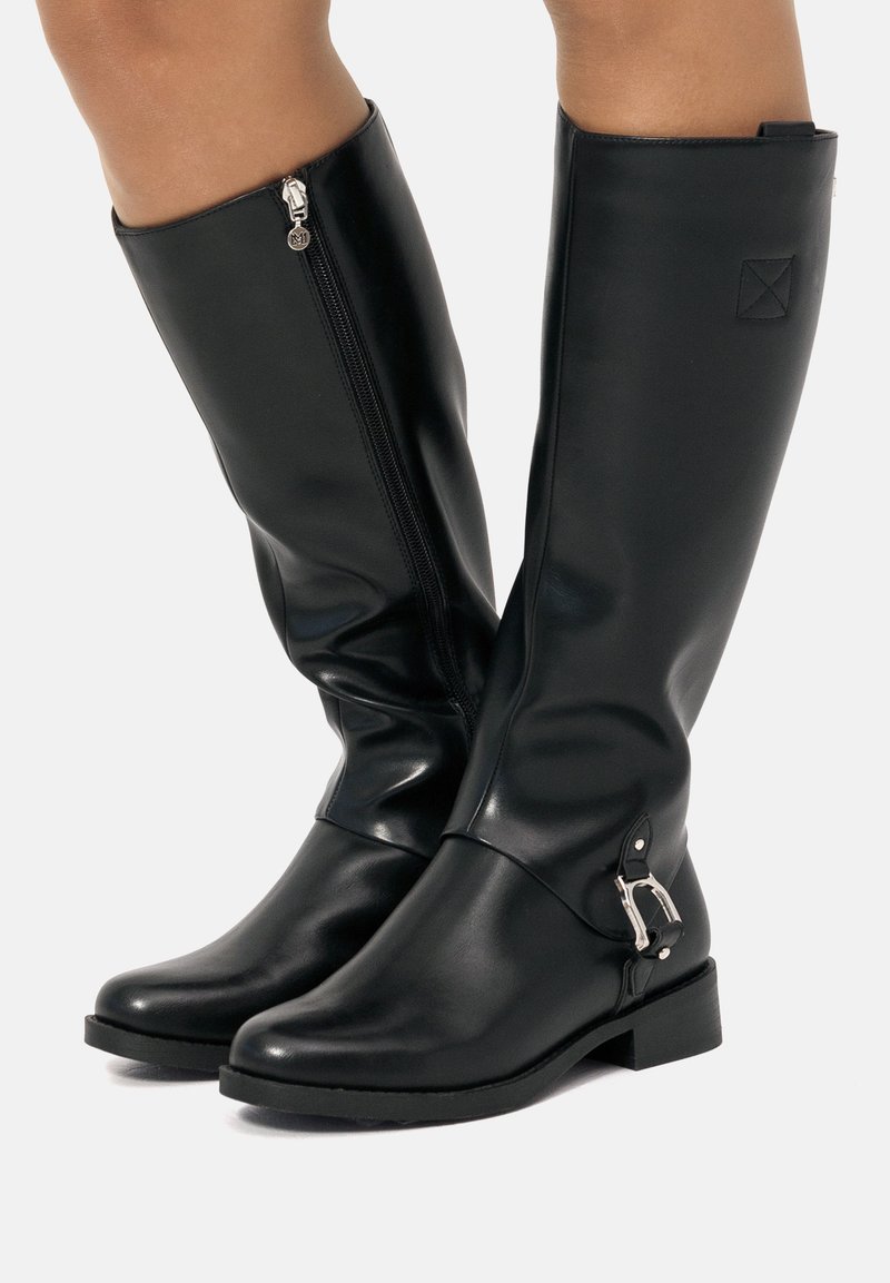 Botas negras hasta la rodilla hechas de cuero sintético suave. Cuentan con un cierre lateral, un pequeño tacón cuadrado y un acento decorativo de hardware plateado.