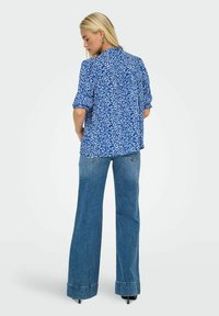 Blå skjorte med hvidt blomstermønster, korte oprullede ærmer og en afslappet pasform. Kombineret med højtaljede denim flared bukser.