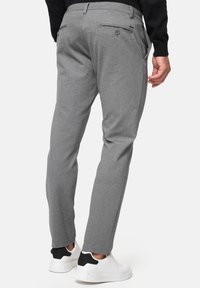 Pantalons gris ajustés avec des jambes fuselées, dotés de poches arrières et d'un tissu texturé. Associés à des baskets blanches et un haut noir.