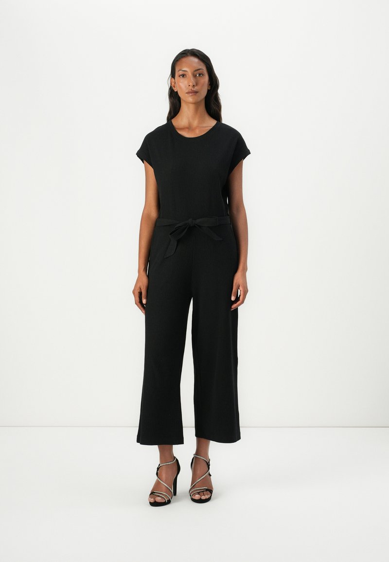 Svart jumpsuit med korte ermer og belte i midjen. Laget av teksturert stoff, med brede ben. Brukt med svarte høyhælte sandaler med stropper.