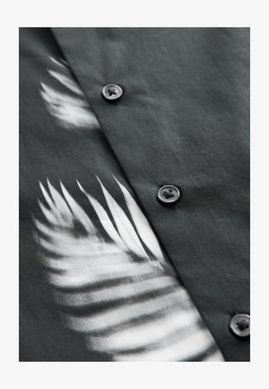 Cămașă cu nasturi din material negru, având un imprimeu alb cu frunze de palmier. Include nasturi închiși la culoare și o textură netedă, mată.