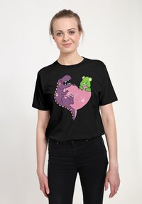 Camiseta negra que presenta un dinosaurio púrpura y un oso verde dentro de un corazón rosa, con detalles juguetones y expresiones caricaturescas.