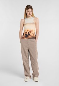Das Tanktop hat ein Farbverlauf-Design mit einem Pferdesilhouetten-Muster in warmen Tönen, kombiniert mit beigen, vertikal gestreiften weit geschnittenen Hosen.