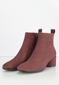 Botas de tobillo de ante marrón con punta redondeada, cierre de cremallera lateral y un tacón bajo. Textura suave con un diseño minimalista.