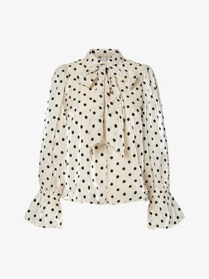 Tej bézs blúz fekete pöttyökkel, masni nyakkal és hosszú puffos ujjakkal, amelyeken bővülő mandzsetta található; sima, fényes anyagból készült.