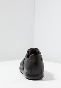 Black leather shoe with a textured knit design on the side, rounded heel, and a smooth surface. Simple, low-profile silhouette.