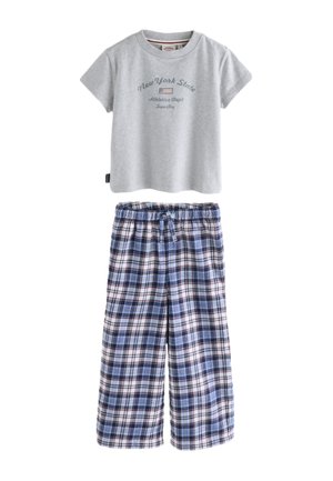 Hænder holder ternede blå og hvide pyjamasbukser med et Superdry-mærke under en grå top og en cremefarvet strikket sweater.