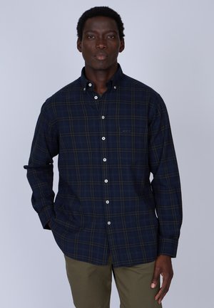 Chemise à carreaux bleu marine, boutonnée, en coton avec des boutons blancs et un logo discret sur la poitrine gauche. Manches longues avec poignets boutonnés.