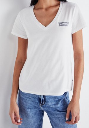 T-shirt blanc à col en V en coton, arborant un logo gris de Levi's sur la zone gauche de la poitrine. Coupe légèrement décontractée et manches courtes.