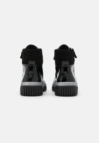 Zapatillas altas negras con acabados de charol brillante y ante, suela de goma resistente y un lazo en la parte posterior para facilitar el uso.
