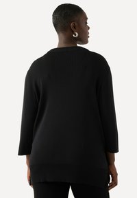 Pull en maille noir avec une coupe décontractée, des manches larges et une texture côtelée. Il présente un col rond et un ourlet arrière allongé.