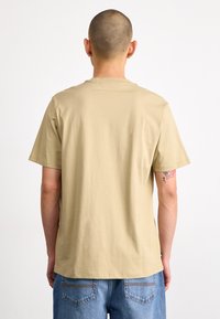 T-shirt beige à manches courtes en coton, présentant une coupe décontractée. Affiche un dos uni avec des coutures minimales et une texture douce.