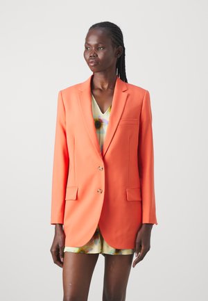 Orange blazer with a structured fit, featuring two front pockets and gold buttons. Worn over a floral-patterned top. Smooth fabric texture.